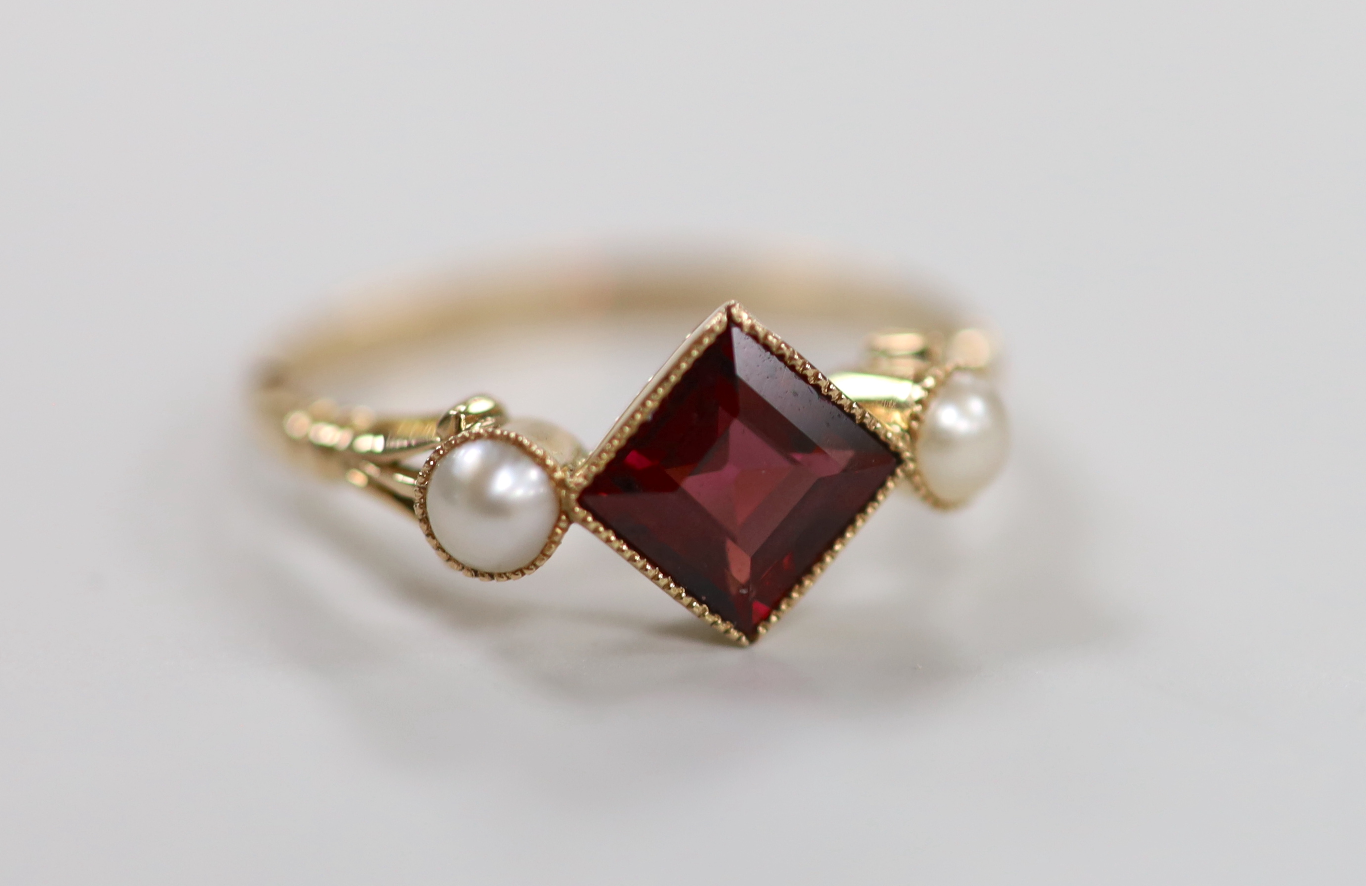 An early 20th century yellow metal, single stone garnet and two stone split pearl set ring, size N, gross weight 2.2 grams.